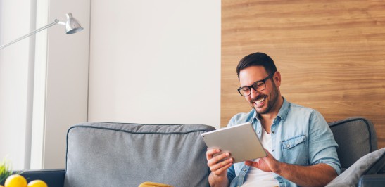 Mann sitzt lachend auf der Couch mit einem Tablet