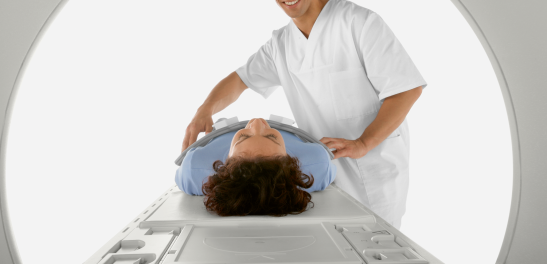 Arzthelfer lächelt Patientin auf der MRT-Liege zu