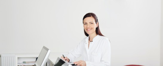 Junge Ärztin lächelt, während sie was am Tresen ausfüllt.